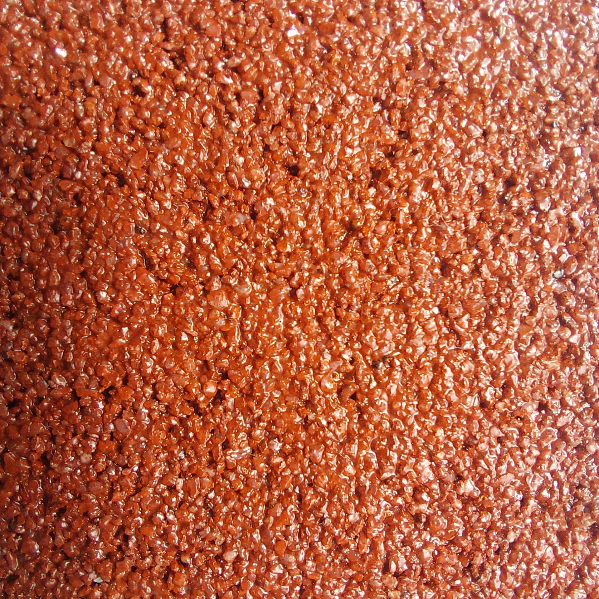 Close-up of a textured red rubber surface, possibly a running track, with small, rounded granules.