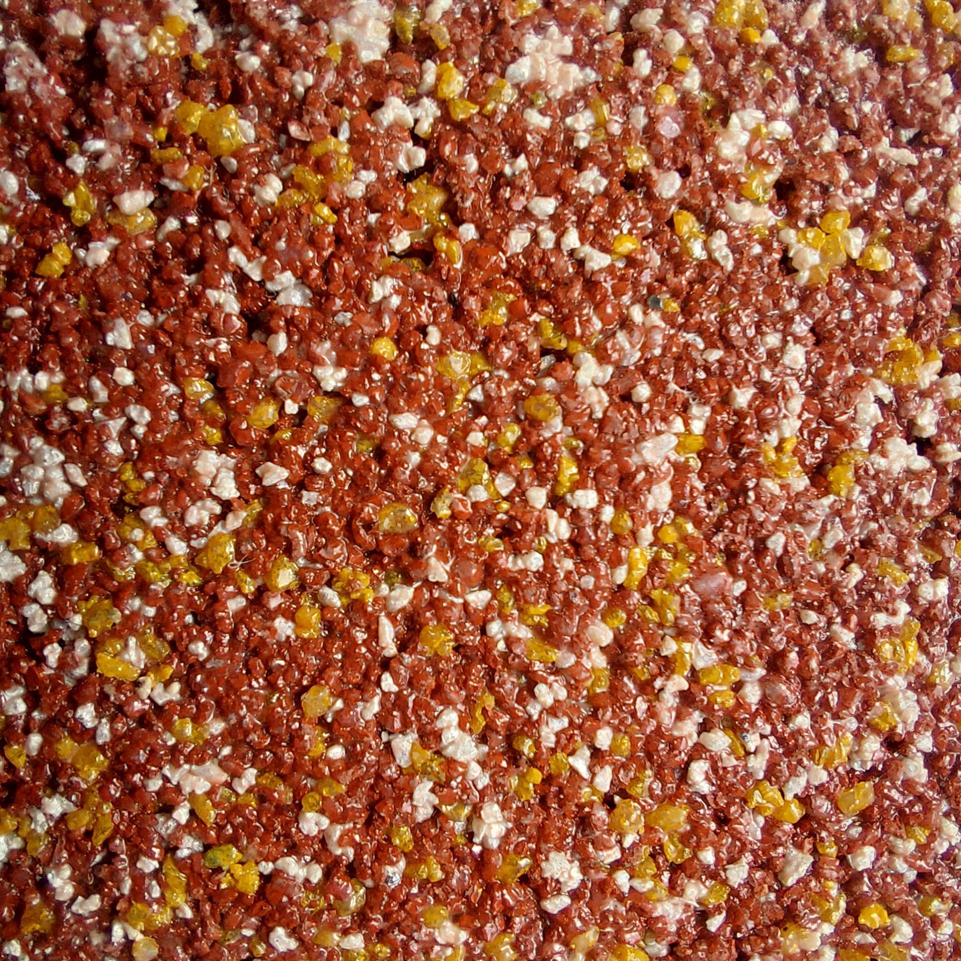 Close-up of a textured surface with small, speckled red, yellow, and white particles.