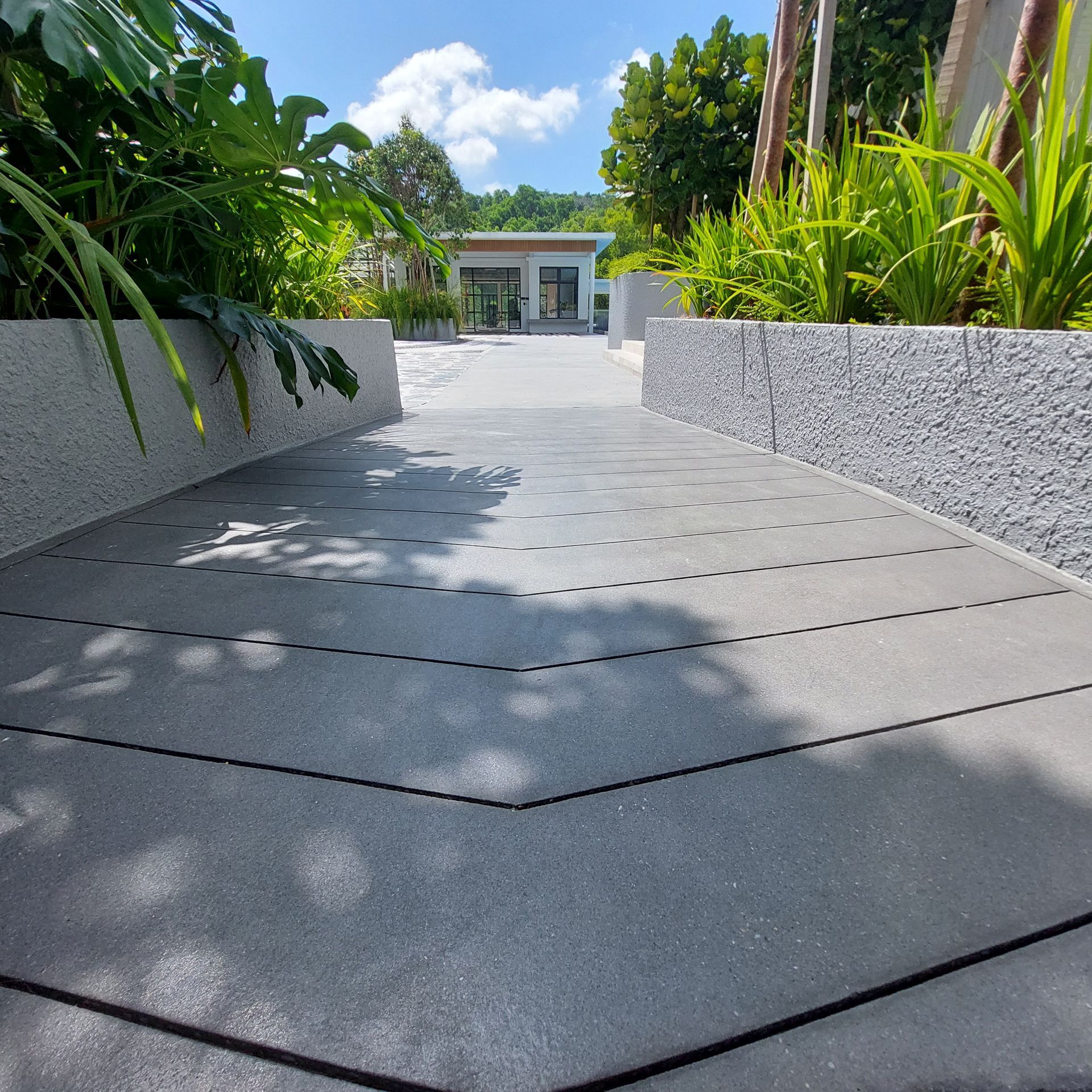 A gray ramp leading to a building, flanked by textured gray walls and greenery, under a blue sky.