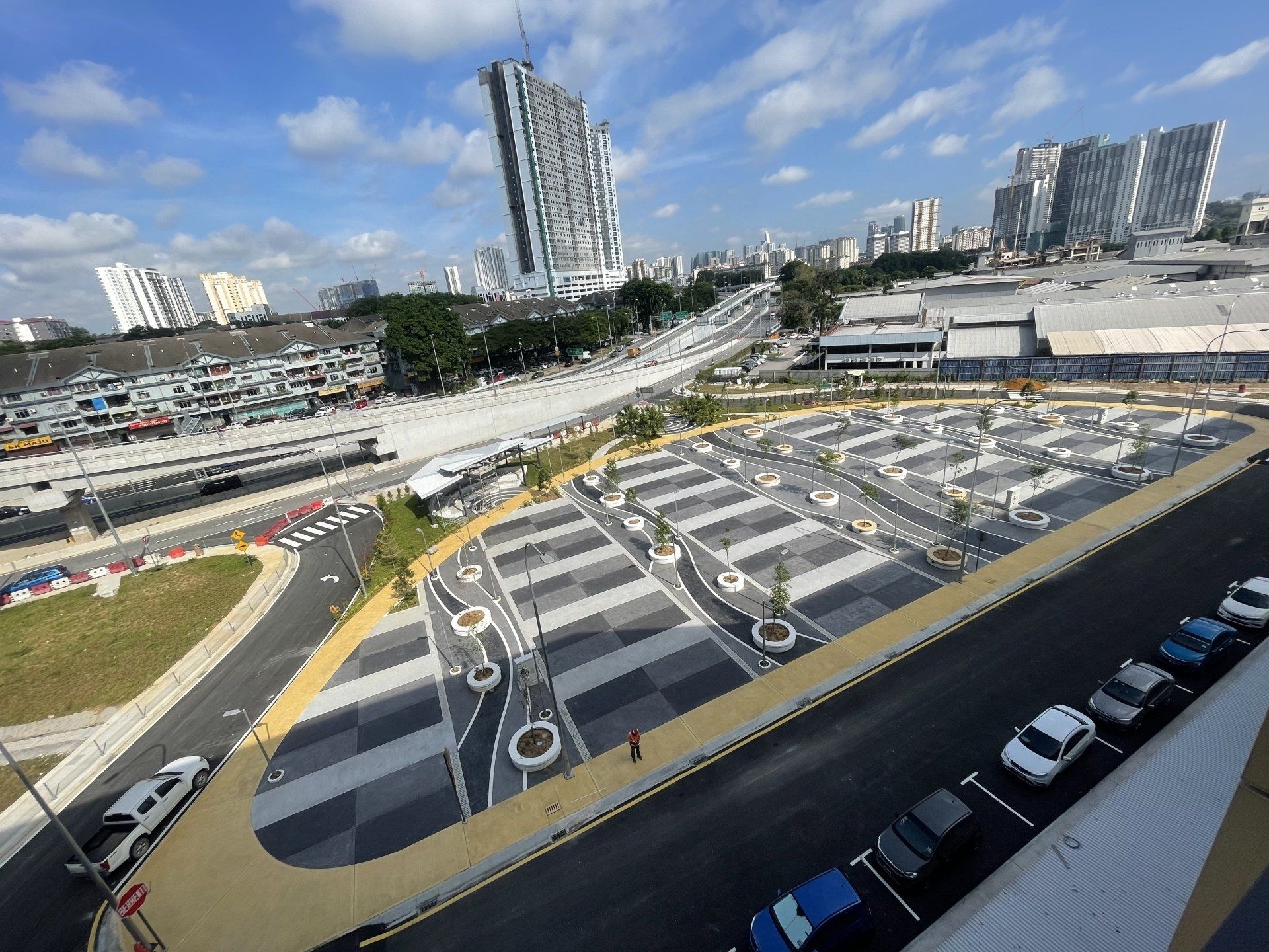 View of a modern bus interchange with rows of parking bays and a tall, angular building in the background.