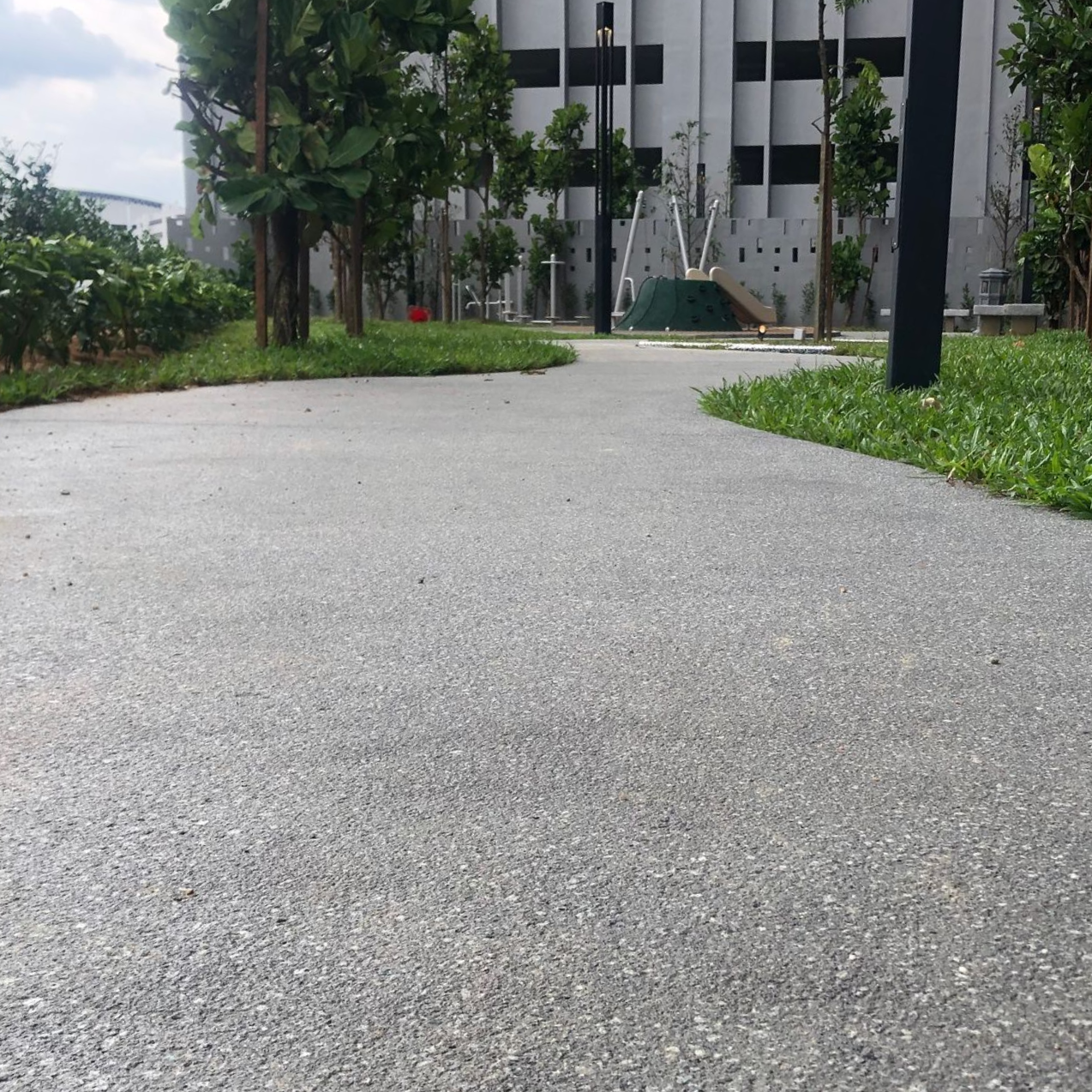 A winding, gray concrete path bordered by grass and trees in a park setting.