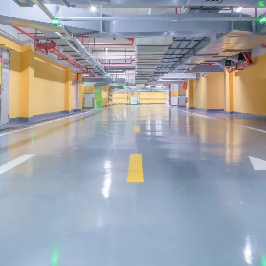 A brightly lit, empty parking garage with yellow walls, gray floor, and overhead pipes and lights.