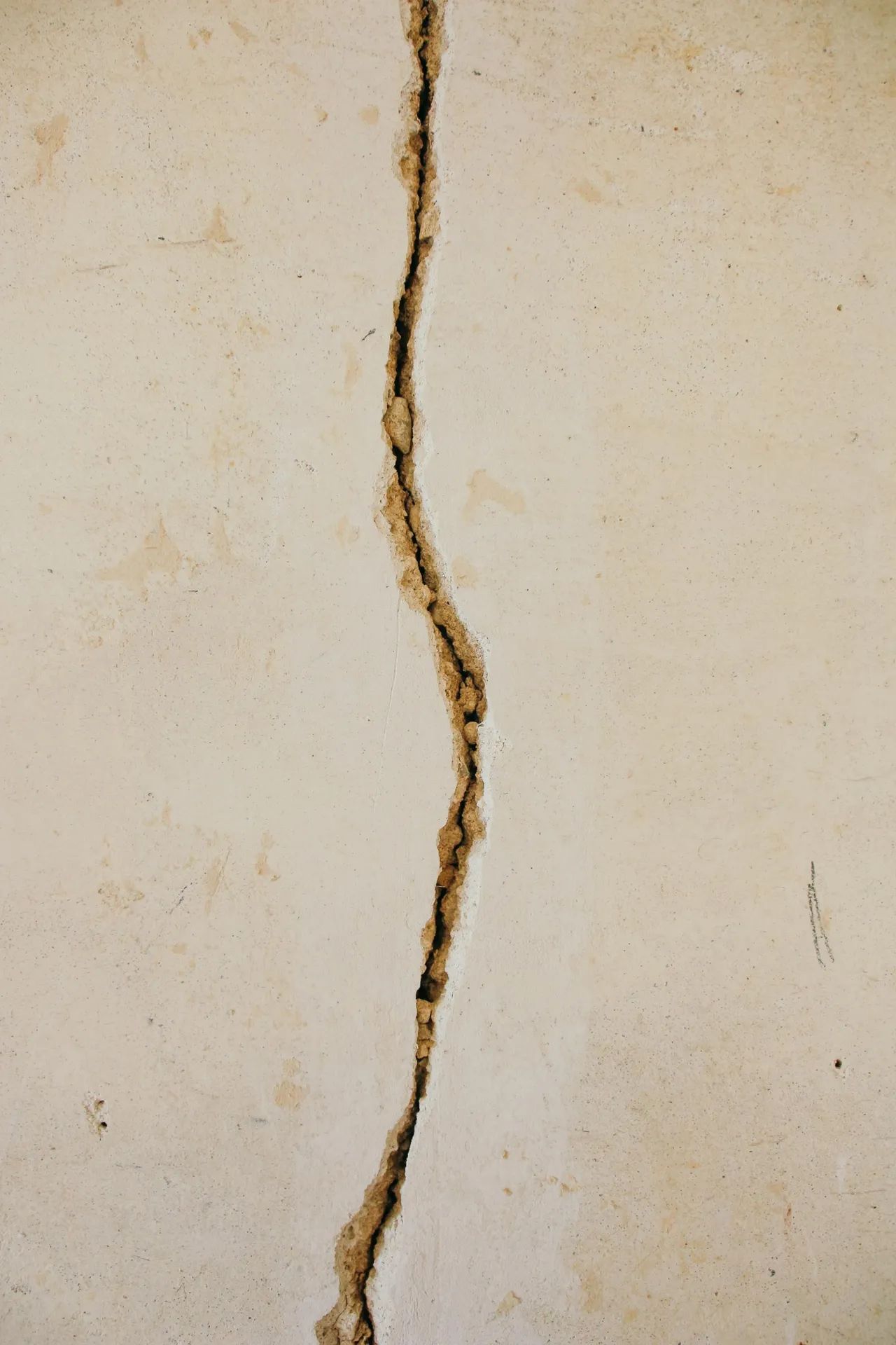 Close-up of a light beige wall with a long, vertical crack running through the center.