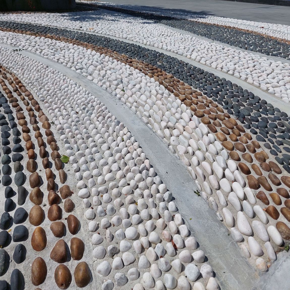 Pebble mosaic pathway with alternating rows of white, brown, black, and gray stones.