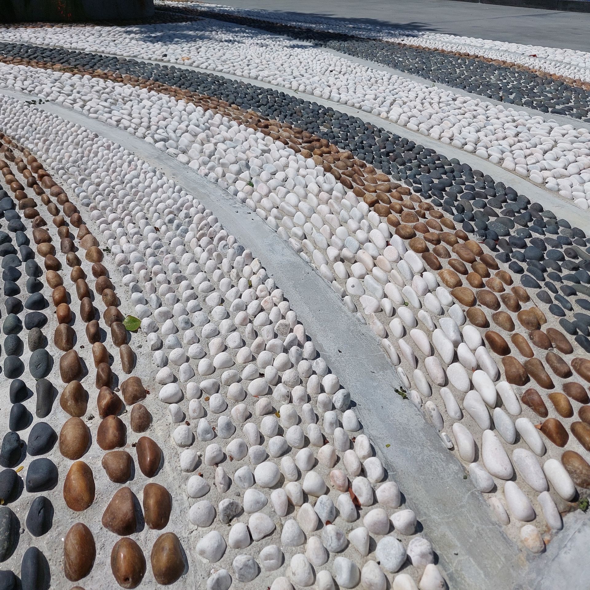 Pebble mosaic pathway with alternating rows of white, brown, black, and gray stones.
