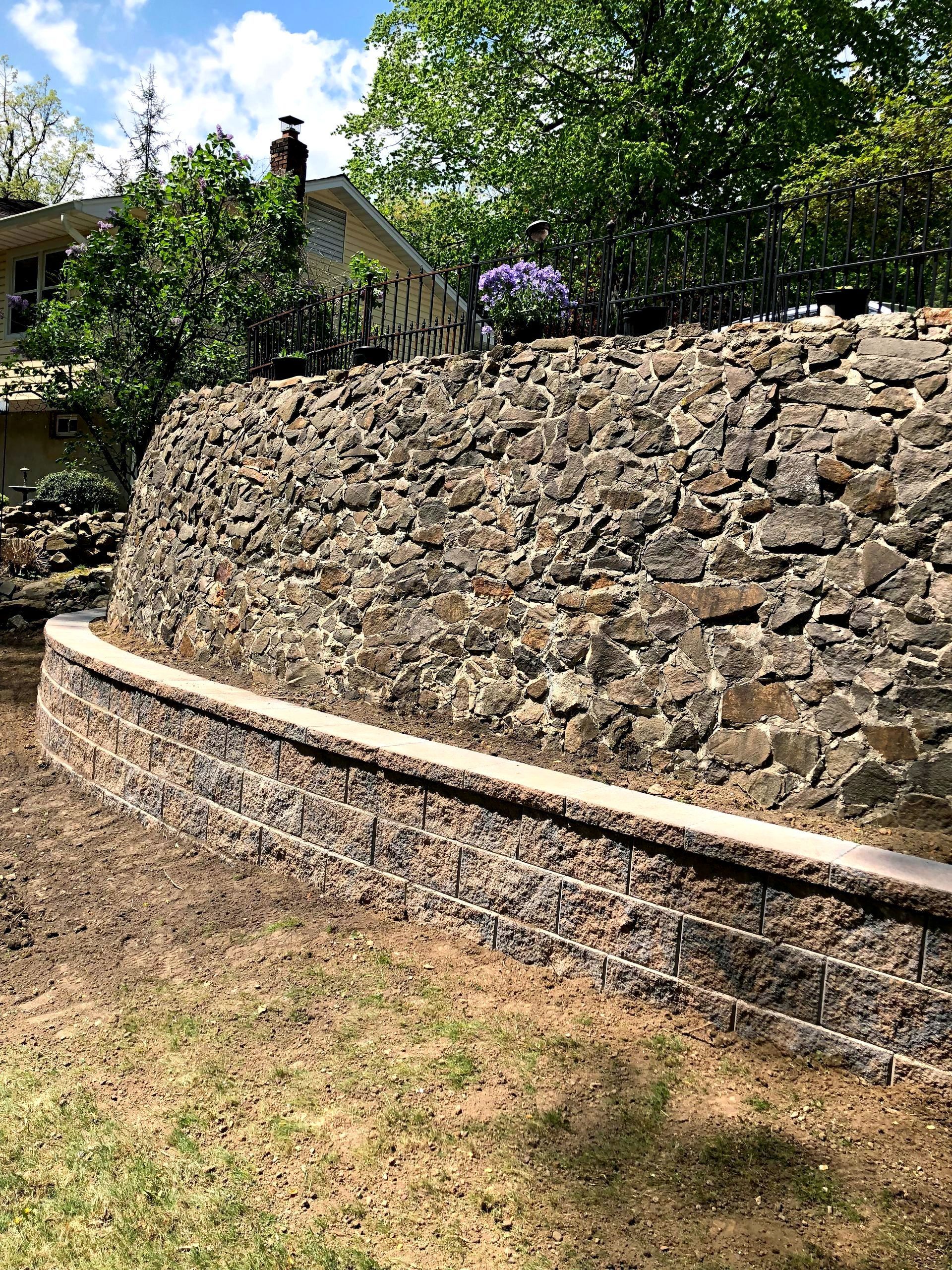 A retainin wall in a backyard with a house in the background.