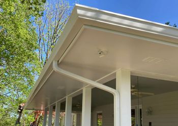 White house porch with columns and rain gutters under a clear blue sky, framed by green trees