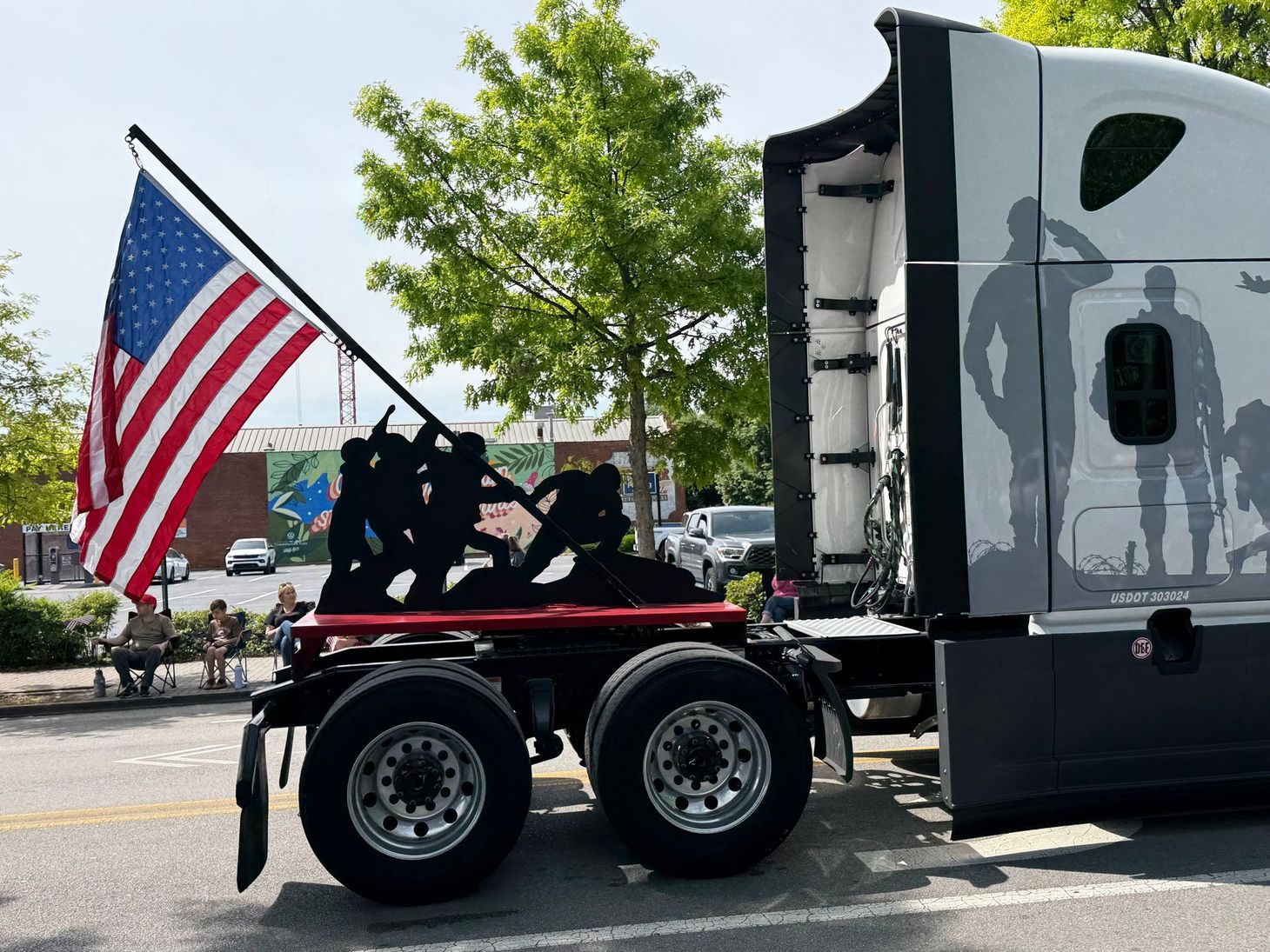 American flag on a black truck cab with large silver trailer in a parking lot