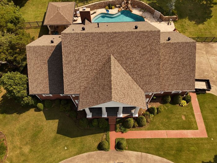 Aerial view of a large house with a pool, driveway, and green lawn