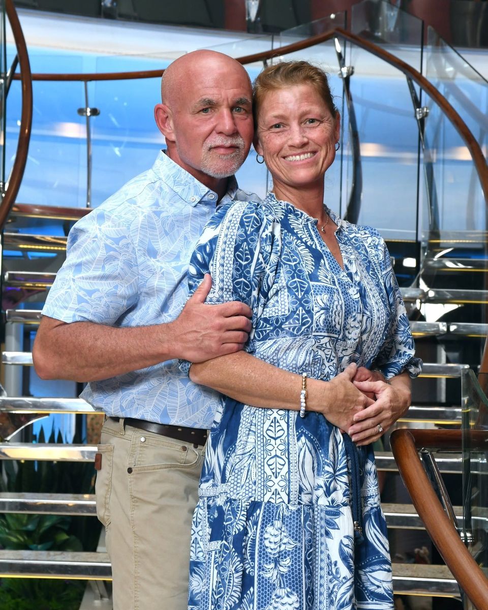 Smiling couple posing together on a ship deck, wearing blue patterned outfits.