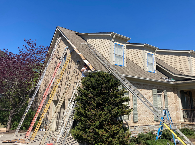 House exterior with a steep roof, multiple ladders, and construction materials leaning against the wall.