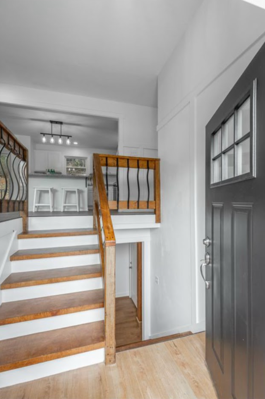 Bright entryway with stairs, wooden railing, dark front door, and light wood floors