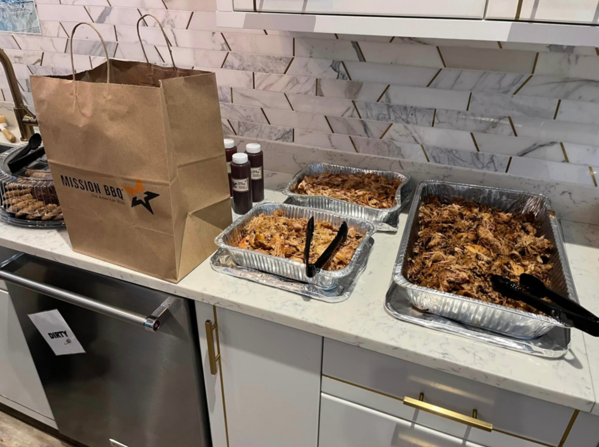 Buffet table with trays of baked dishes and a paper bag in a kitchen setting