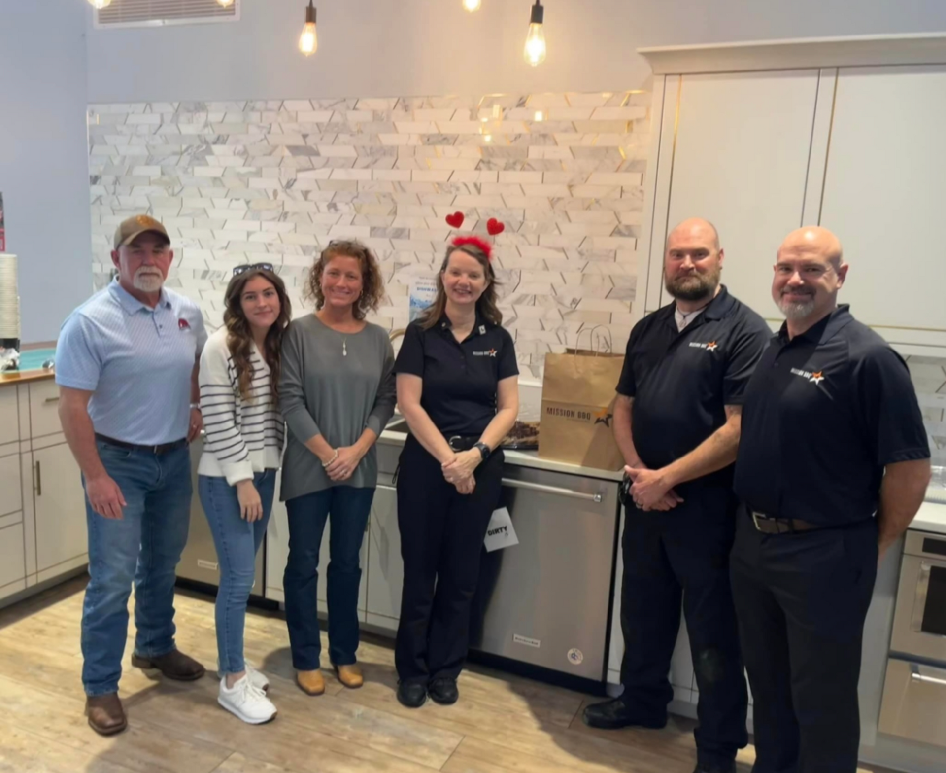 Five people posing in a kitchen showroom, with pendant lights and a stainless dishwasher behind them.