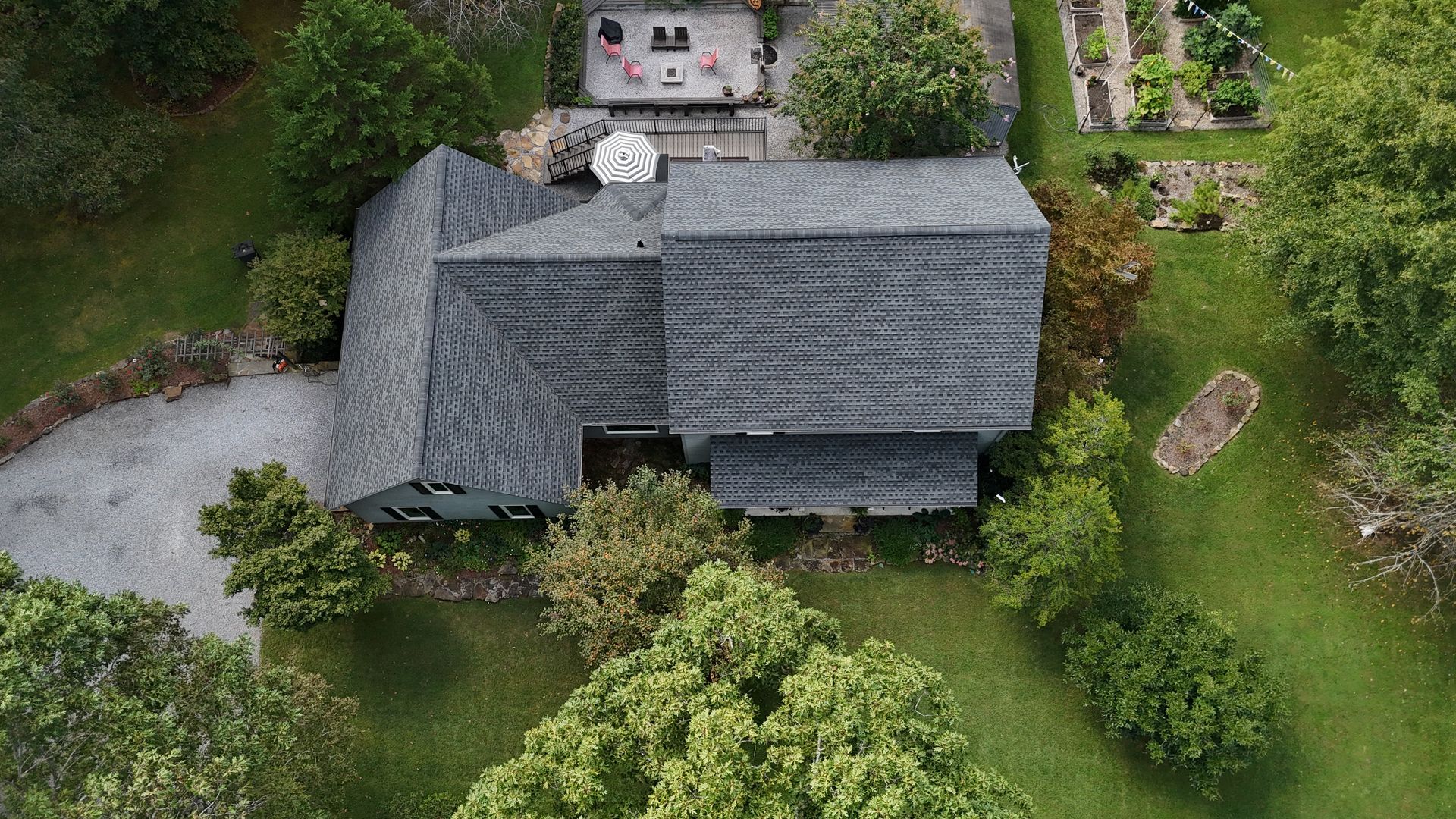 Aerial view of a gray-roofed house surrounded by trees and green lawn.