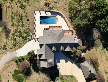 Aerial view of a house with a backyard patio, swimming pool, and surrounding trees