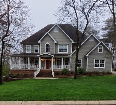 Large gray suburban house with white trim, front porch, and green lawn on an overcast day