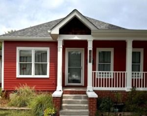 Red house with white trim, front porch, steps, and a central front door.