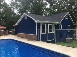 Blue house beside a swimming pool, with a concrete deck and chain-link fence