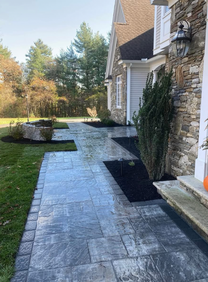 Stone walkway leading to a house with a stone and wood exterior; landscaping and grass on either side.