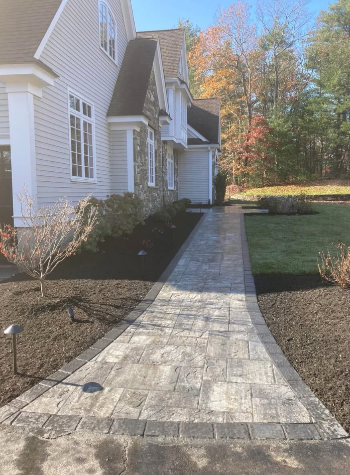 Stone walkway leading to a light gray house with dark brown trim and a landscaped front yard.