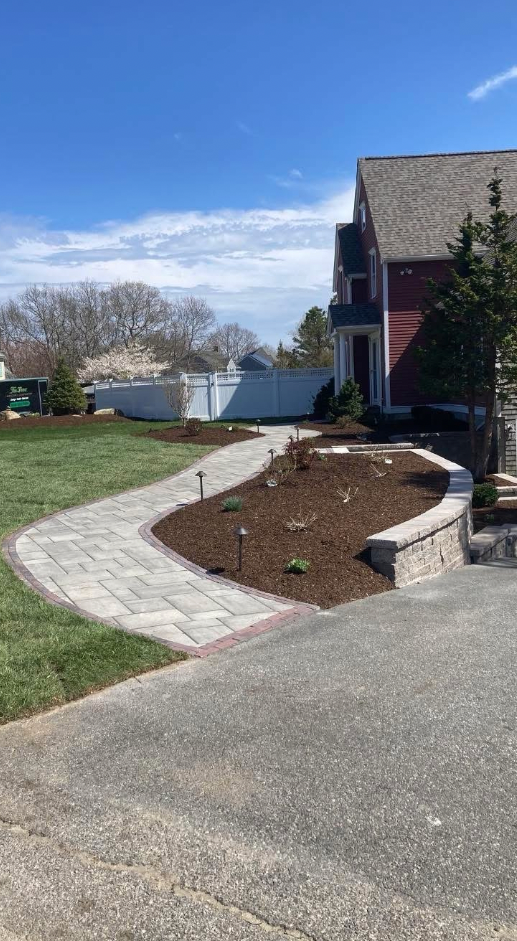 Stone pathway curving to a red house, surrounded by lawn and a retaining wall filled with mulch.
