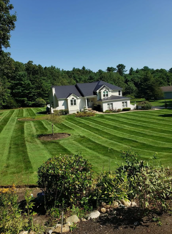 A well-manicured lawn with striped patterns in front of a white house with a dark roof on a sunny day.