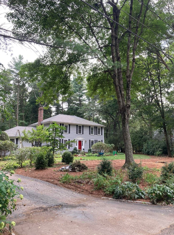 Gray house with red door, surrounded by trees and a garden.