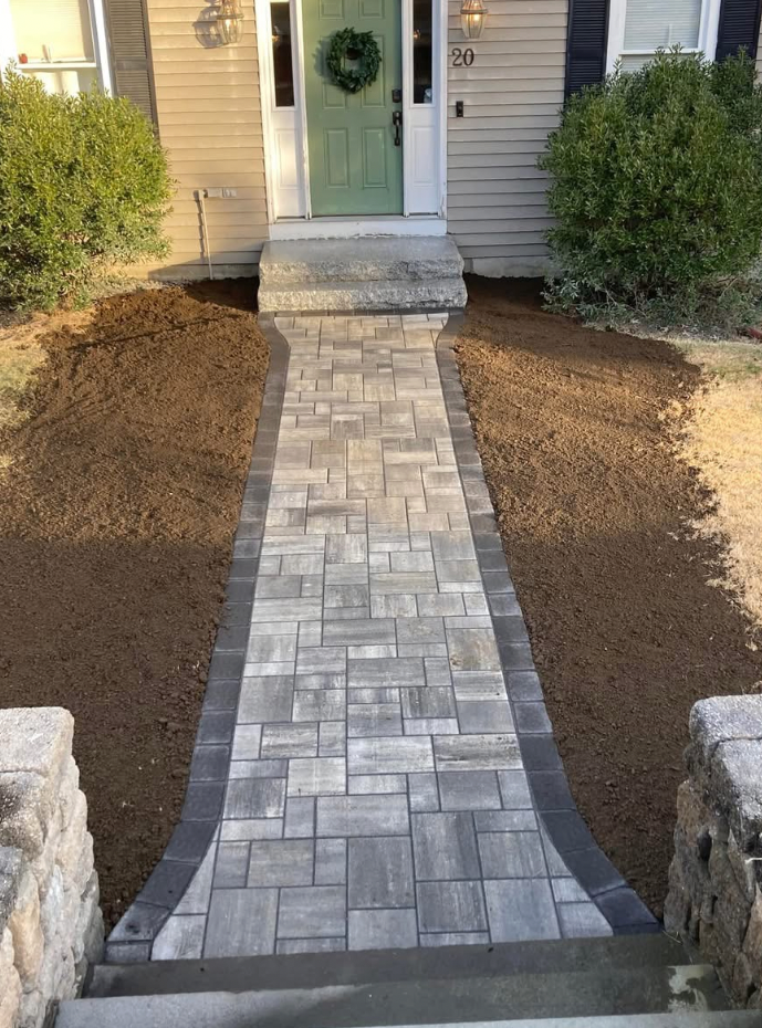 Brick walkway leading to a house with a green door, flanked by bushes and mulch.