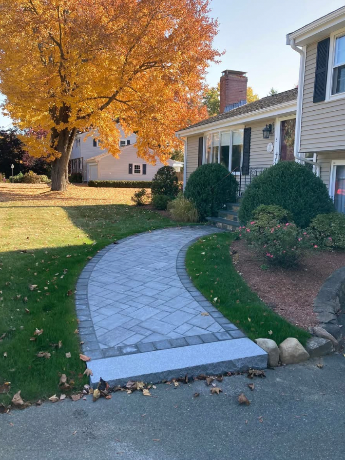 Brick walkway leading to a beige house with autumn foliage.