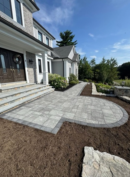 Gray paver patio and walkway leading to a two-story house with blue sky background.