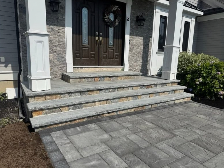 Gray stone steps leading to a brown double door entrance, flanked by white columns and a gray stone wall.