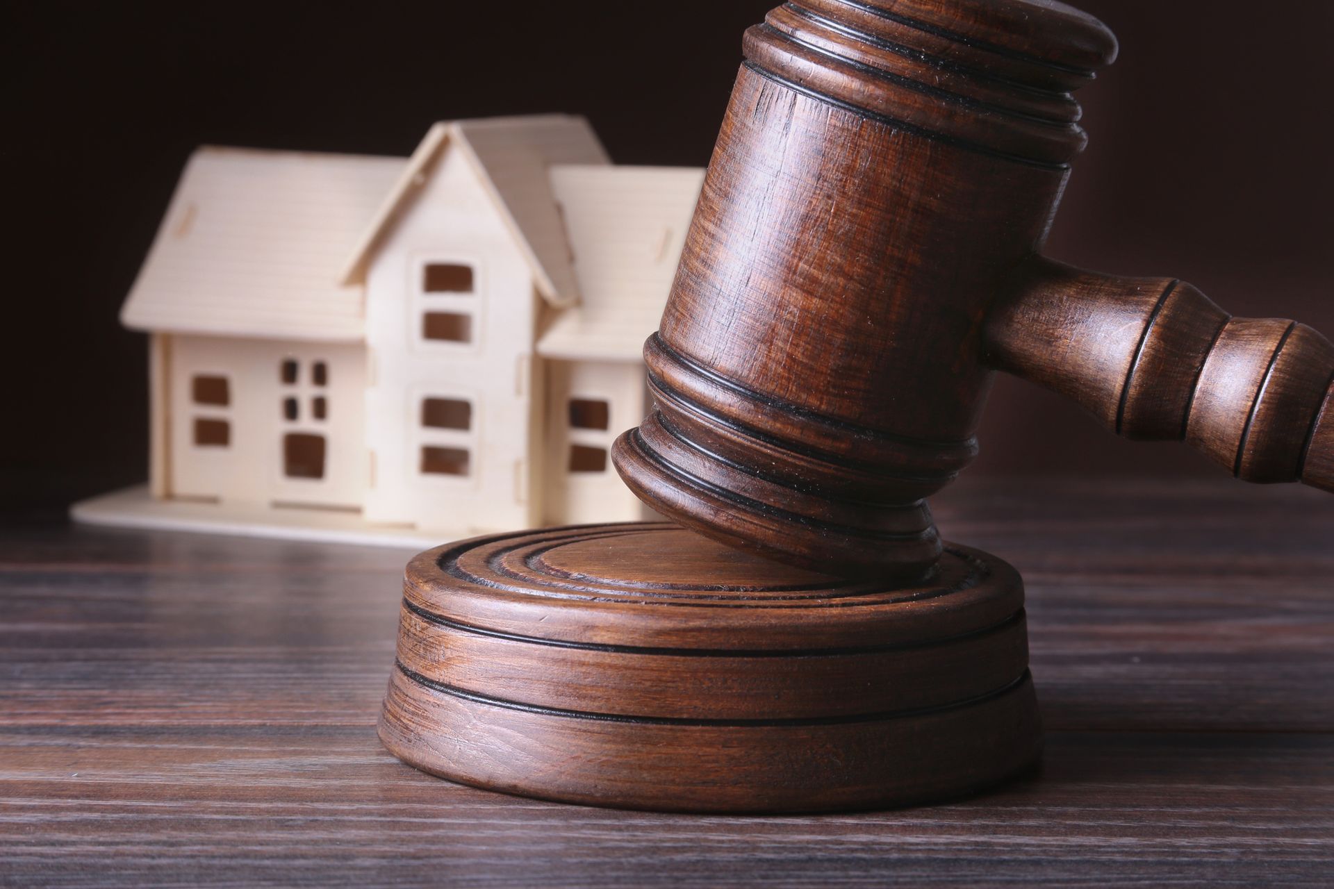 A house model and a judge's gavel are placed on a wooden table, highlighting the role of auctioneers