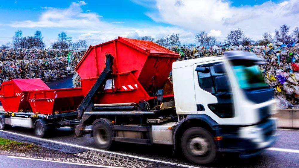 A Dump Truck is Driving Down a Road Next to a Pile of Trash — Handi Skips in Bohle, QLD