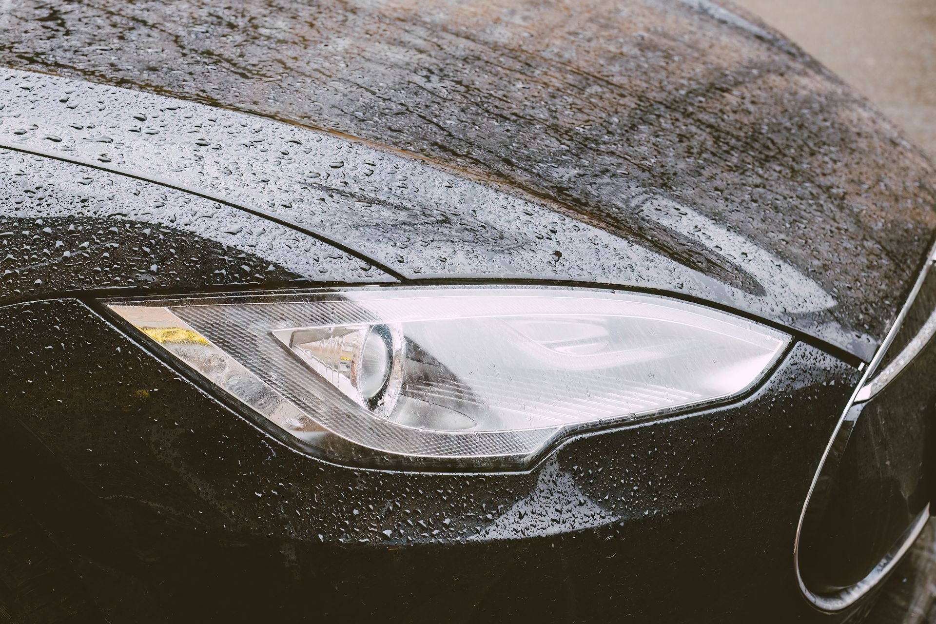 Rain-covered black car headlight close-up