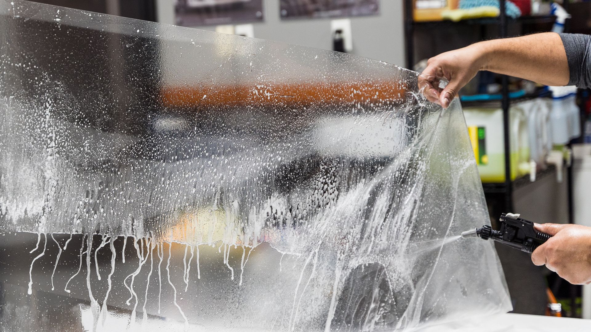 Person spraying water from a hose onto a car, creating a mist in an outdoor cleaning area