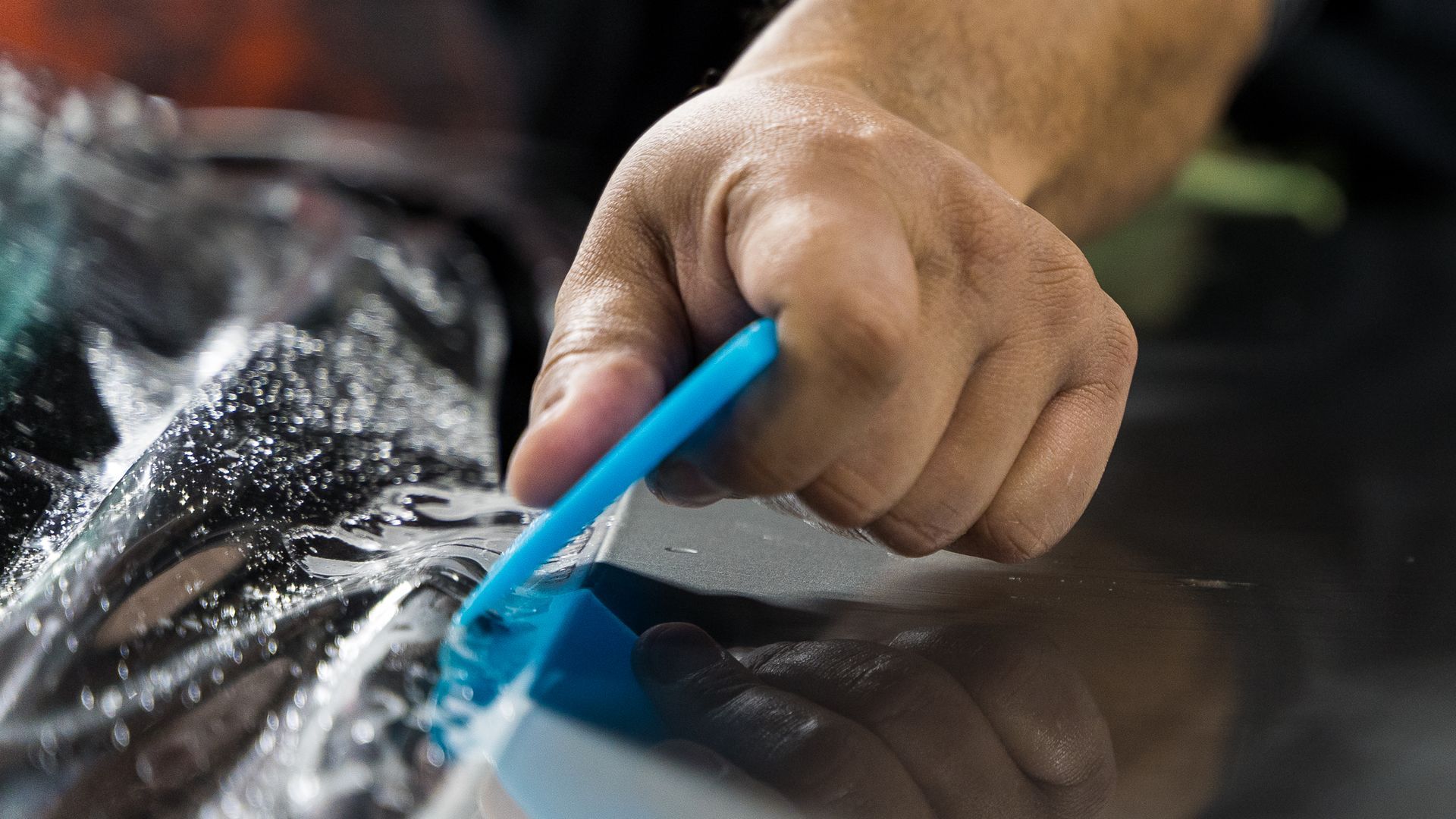 Hand using a blue squeegee to clean a wet car windshield