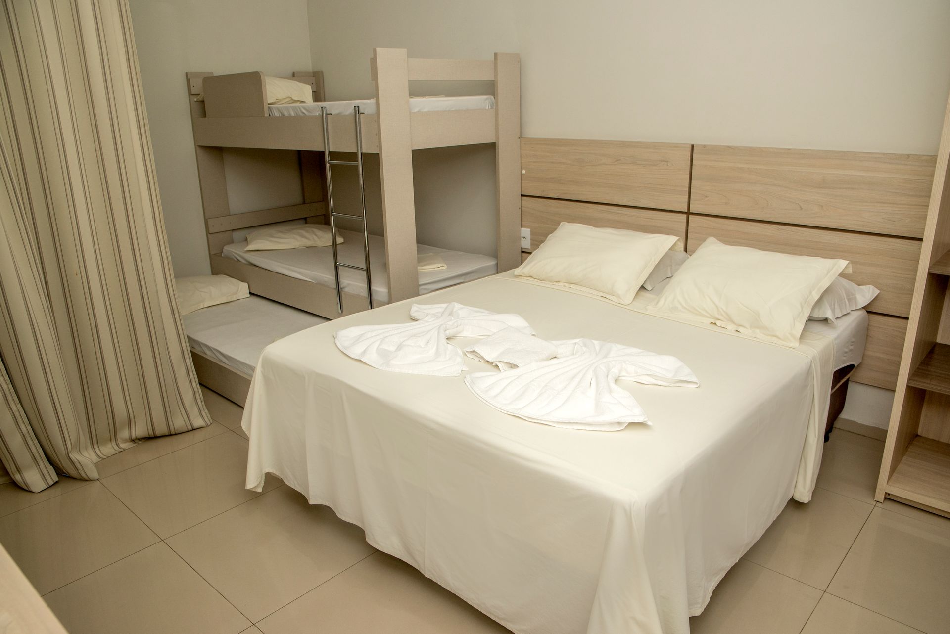 Quarto impecável com cama de casal, beliches, lençóis brancos e piso de azulejo.