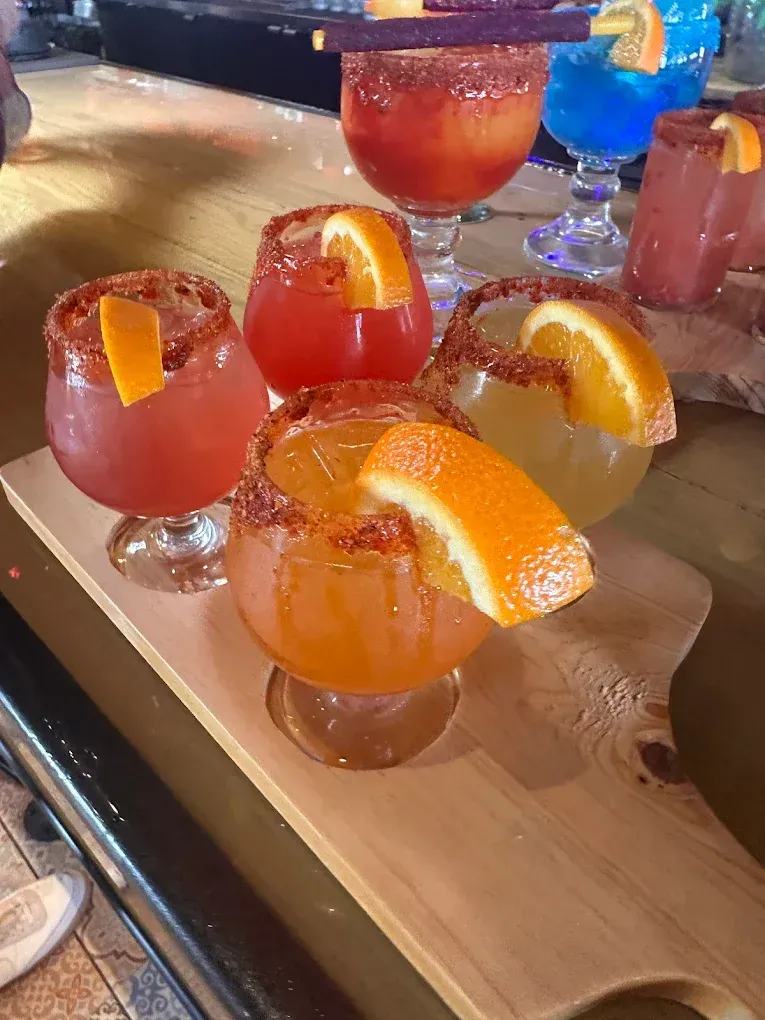 Assorted colorful cocktails garnished with orange slices on a tray at a bar