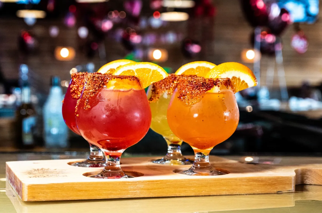 Two colorful cocktails with orange slices on a wooden board at a bar