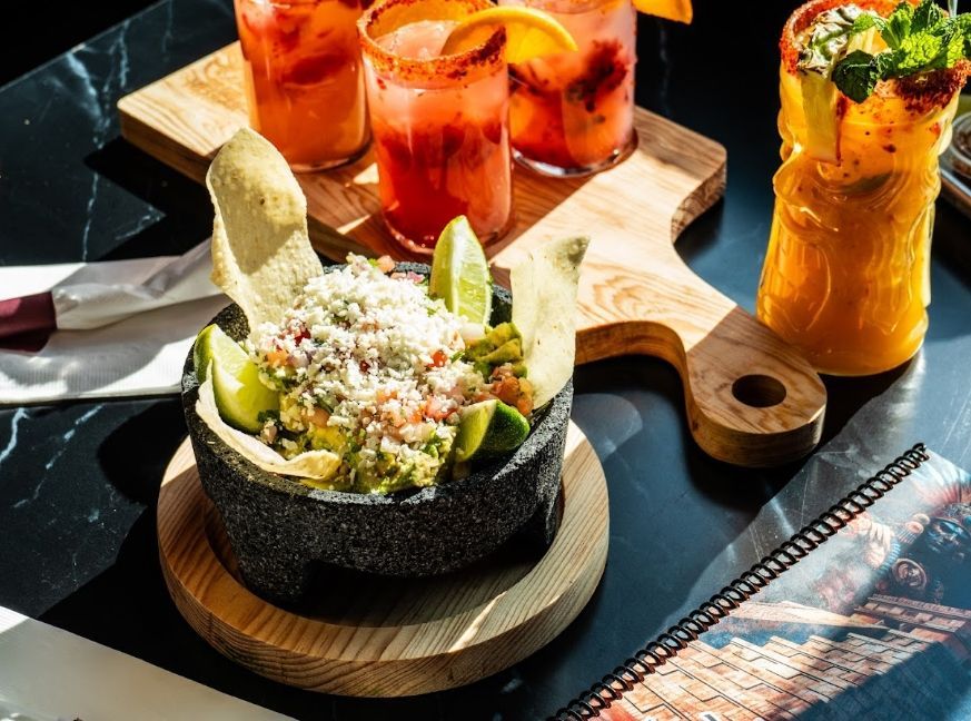 Tortilla bowls with fresh Mexican dishes and colorful cocktails on a wooden serving board