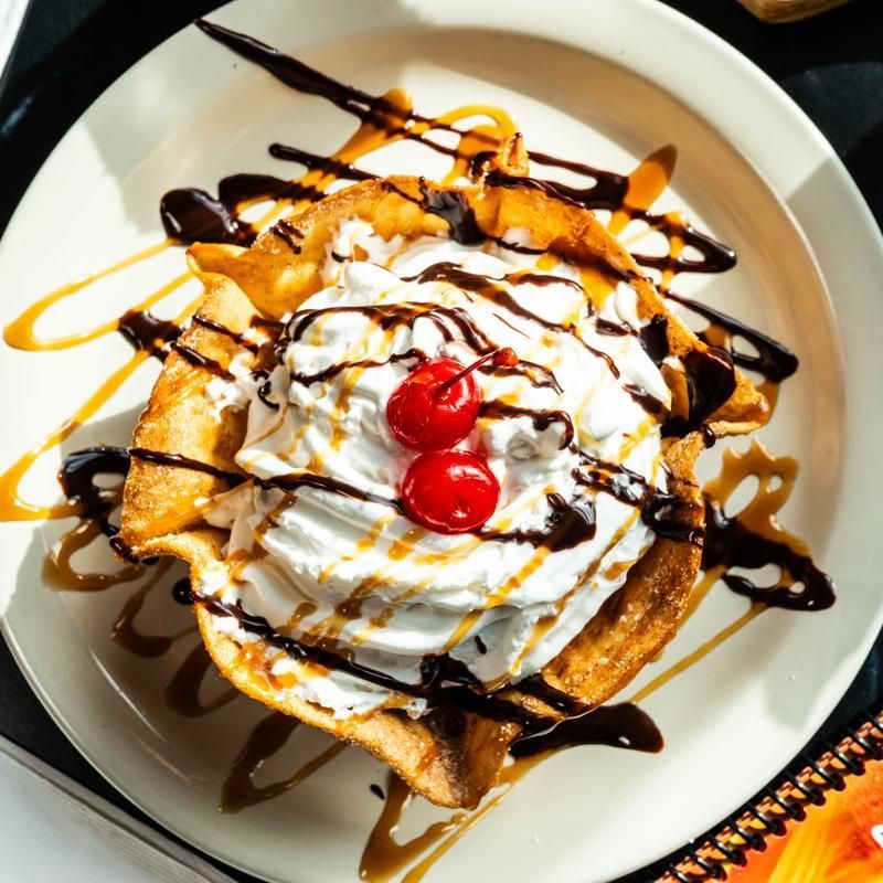Dessert waffle topped with whipped cream, cherries, and chocolate sauce on a white plate