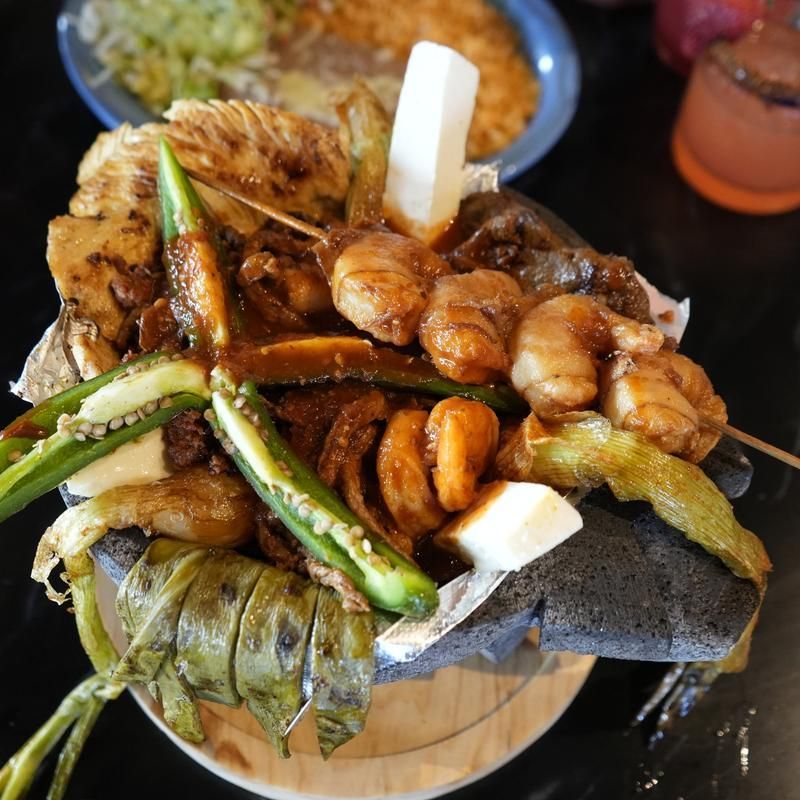 A stacked platter of fried seafood and vegetables on a dark table, with a dipping sauce in the background