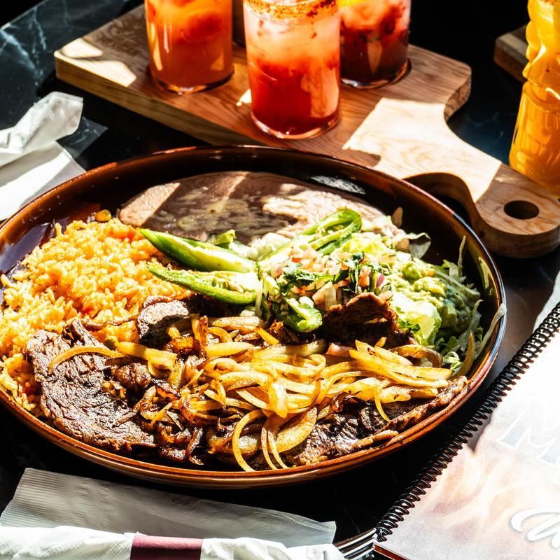 Mexican meal platter with rice, beans, vegetables, and three drinks on a wooden tray
