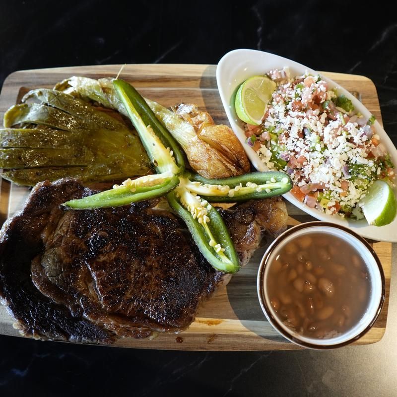 Barbecue platter with grilled meats, nopales, rice, beans, and tortillas on a wooden tray
