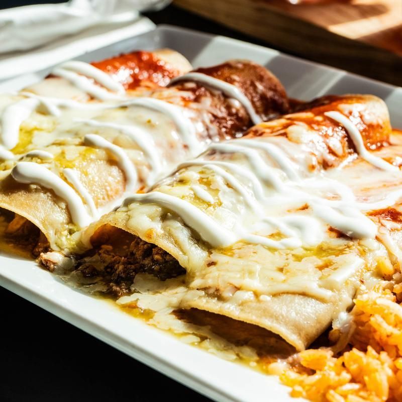 Three enchiladas topped with melted cheese and sauce on a white plate