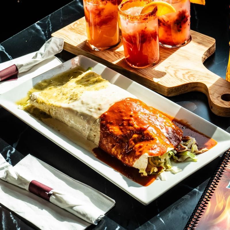 Enchiladas and rice on a white plate with salsa, beside three drinks on a wooden tray.