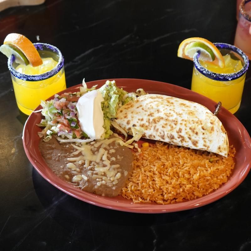 Mexican meal platter with tacos, rice, refried beans, and two orange drinks with lime slices