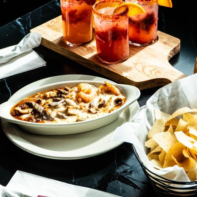 Table with a baked dish, chips, and three red cocktails on a wooden tray