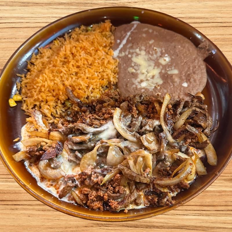 Plato de comida mexicana con carne, cebolla, arroz rojo y frijoles refritos en una bandeja ovalada.